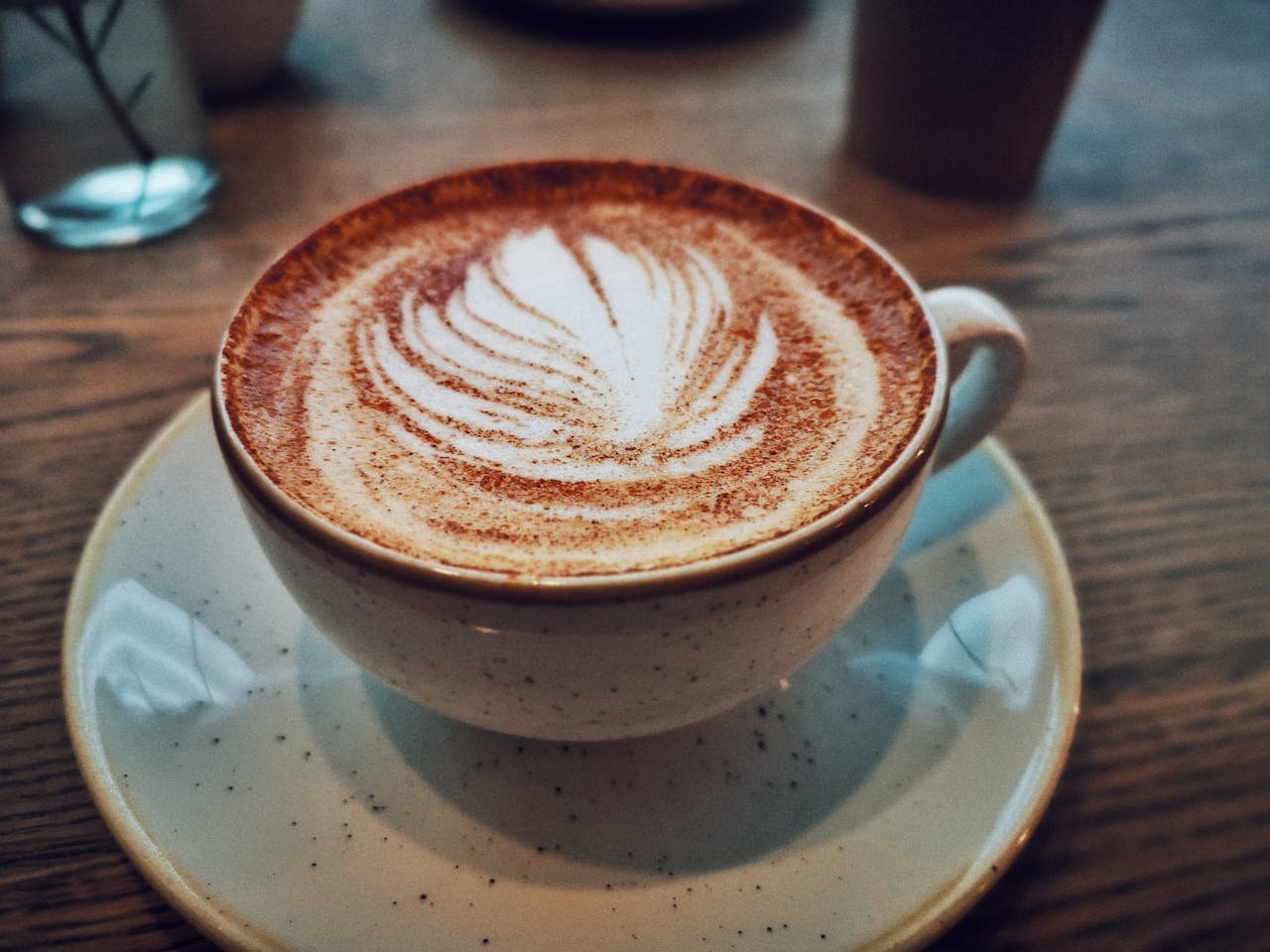 Close-up of a cappuccino with detailed latte art in a cozy cafe setting.